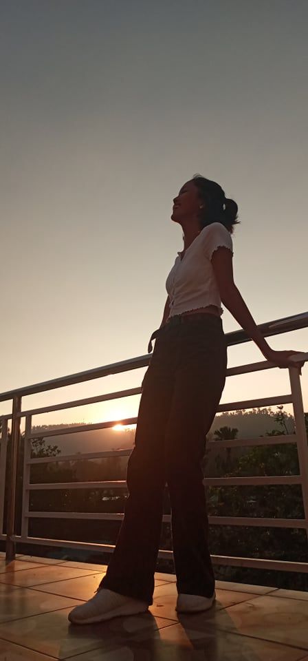 a woman standing on top of a balcony next to a railing with the sun setting in the background