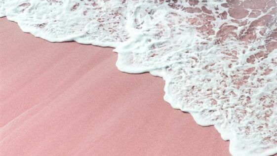 an aerial view of the ocean waves and pink sand