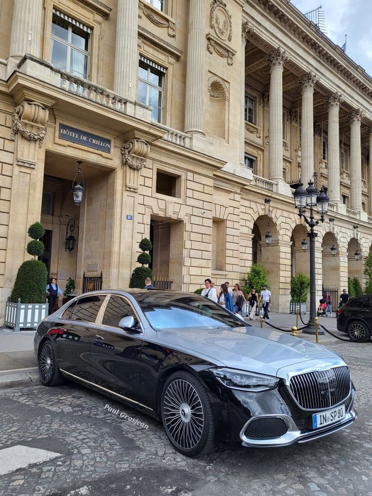 a black car parked in front of a large building with columns on it's sides