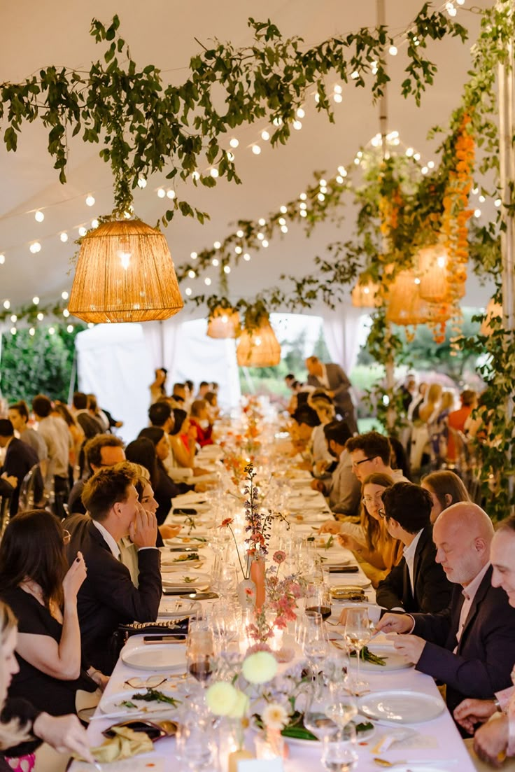 a group of people sitting at a long table in a tent with lights hanging from the ceiling