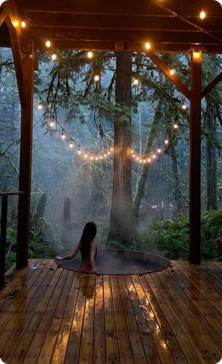 a woman sitting on a wooden deck in front of a tree with lights strung from it