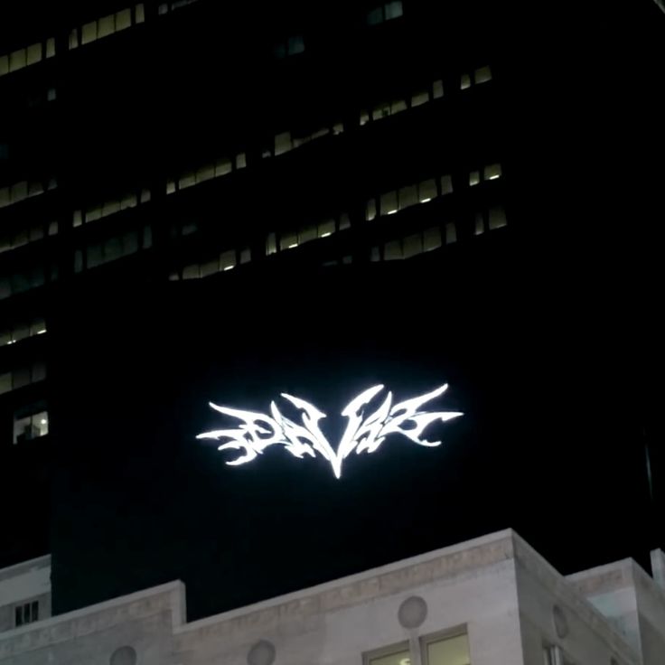 the logo on top of a building in front of a tall building with windows at night