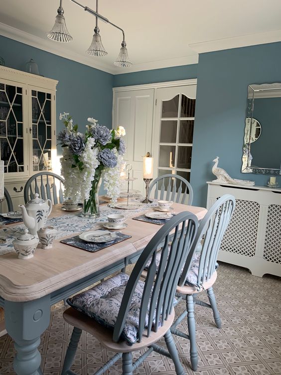 a dining room with blue walls and white furniture in the center, along with flowers on the table