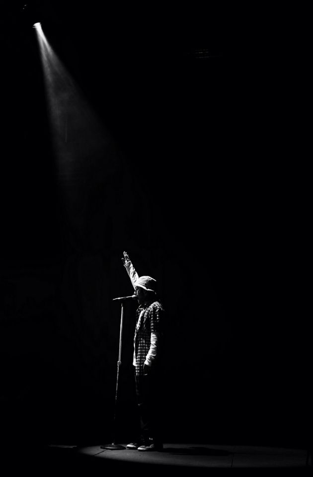 a person standing on a stage with a microphone in front of him and light coming from behind them