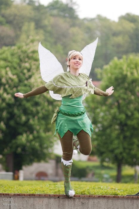 a woman dressed as tinkerbell running on a wall with trees in the background