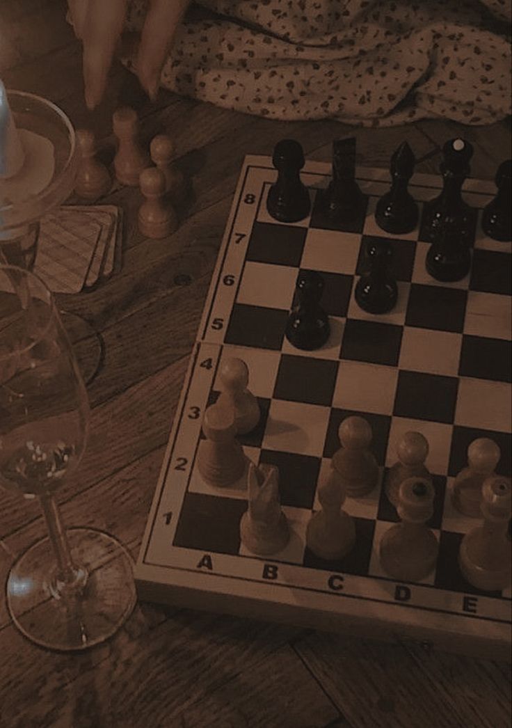 a chess board and some wine glasses on a table in front of a person sitting down