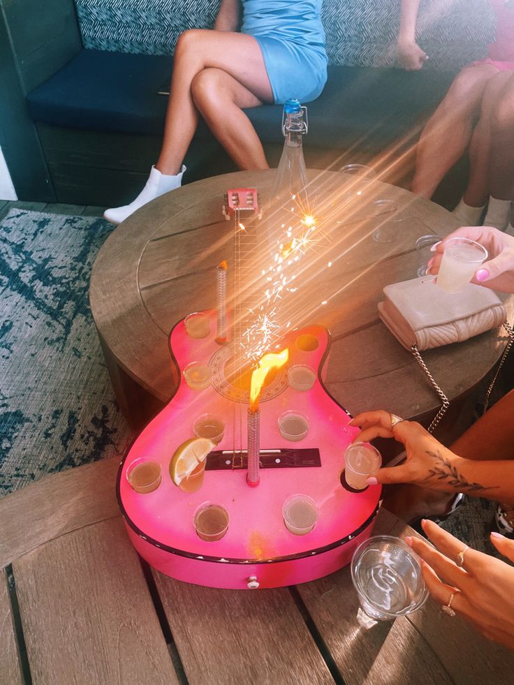 a pink guitar shaped cake sitting on top of a wooden table next to two women