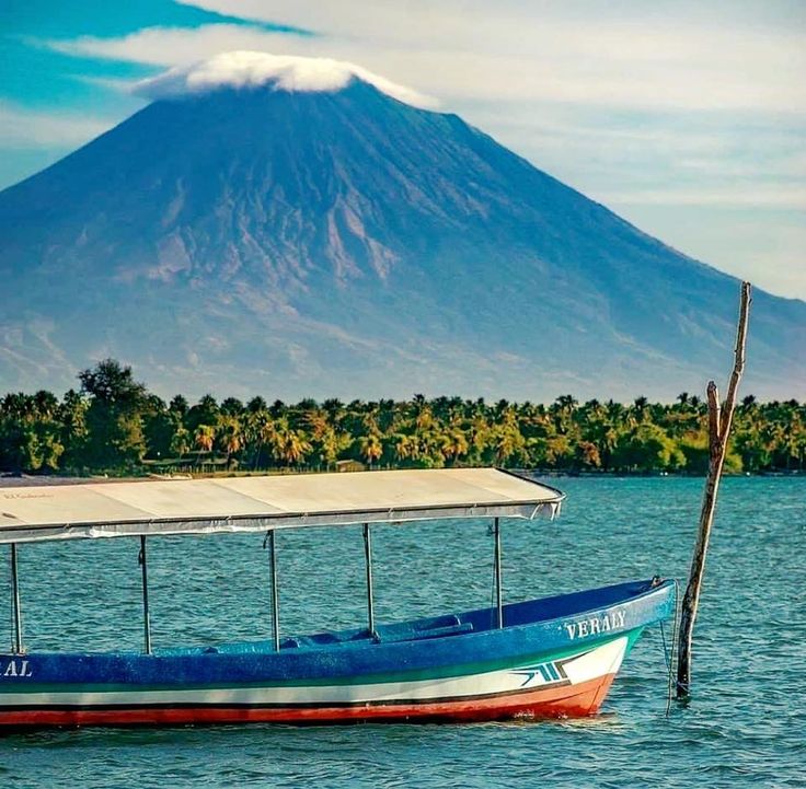 a blue boat floating on top of a lake next to a large mountain in the background