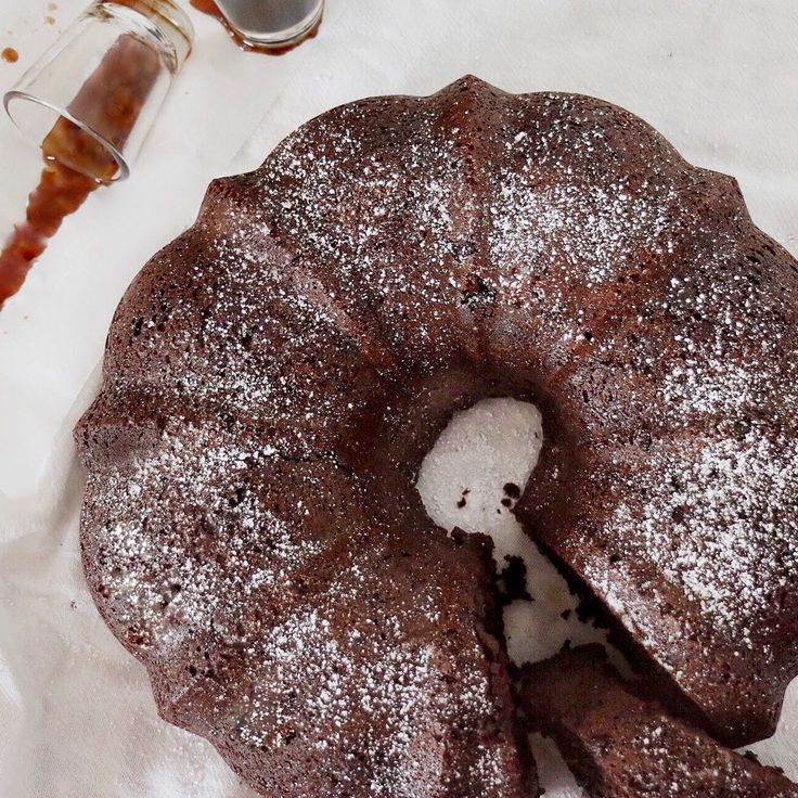 a chocolate bundt cake with powdered sugar on top and syrup in the background