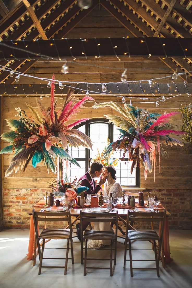 two people sitting at a table with flowers hanging from the ceiling