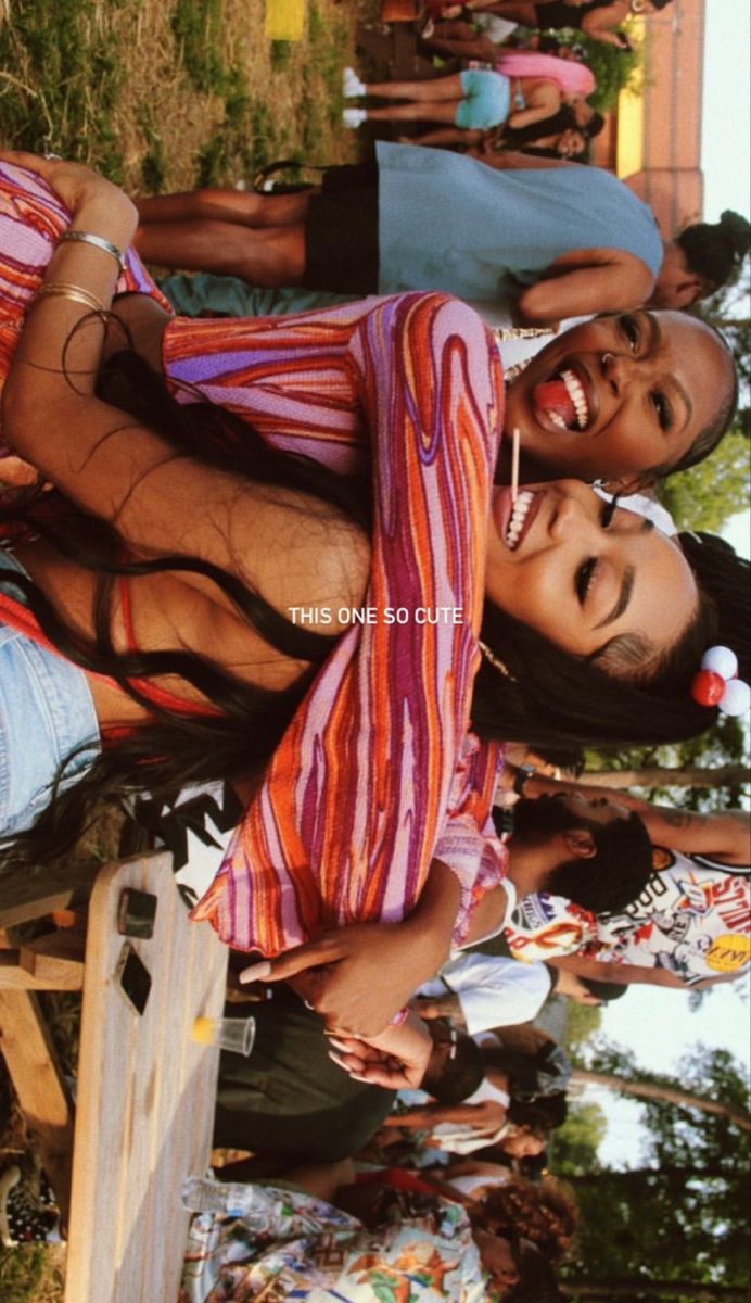 two women are posing for the camera in front of other people and one is wearing a colorful dress