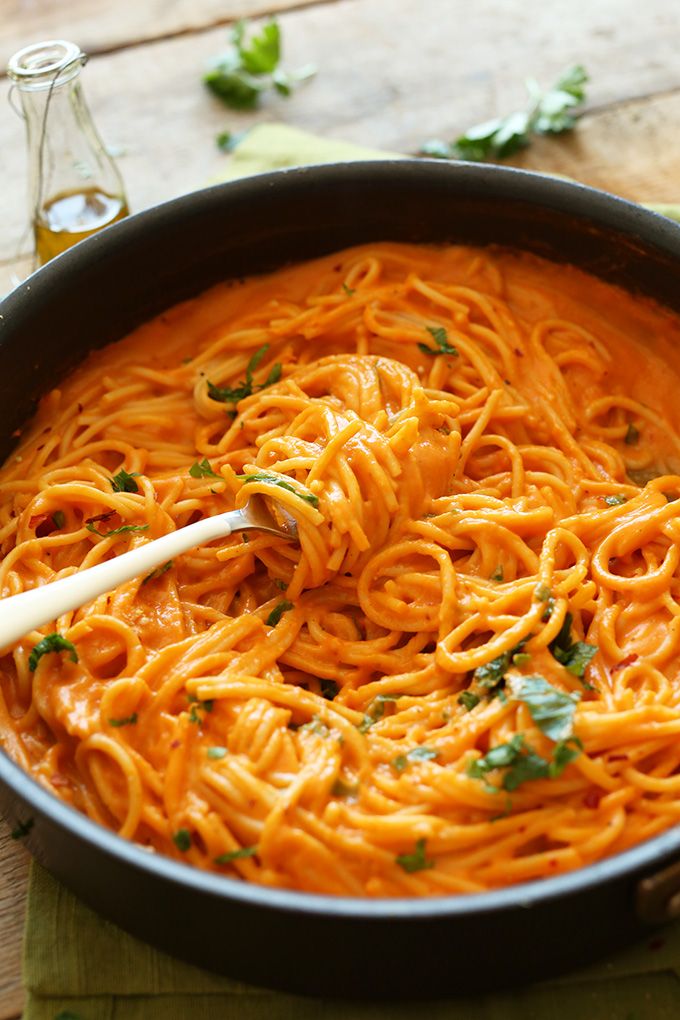 a pan filled with pasta and garnished with parsley on the side, sitting on a wooden table