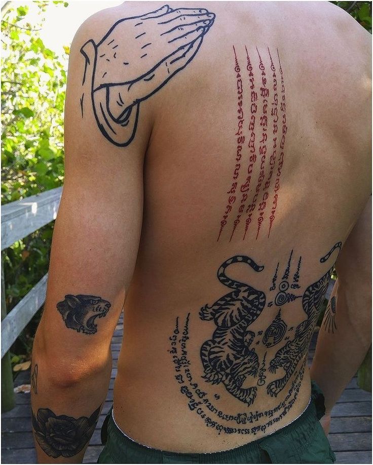 the back of a man with tattoos on his upper and lower half, standing in front of a wooden deck