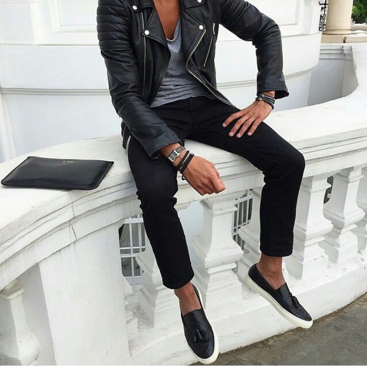 a man sitting on top of a white wall next to a black purse and cell phone