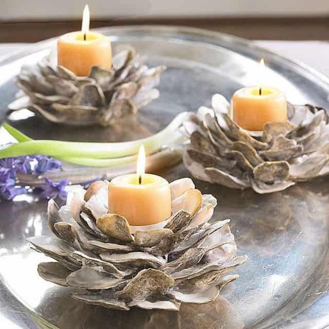 three pine cone candles are on a silver plate with purple flowers and lavenders in the background