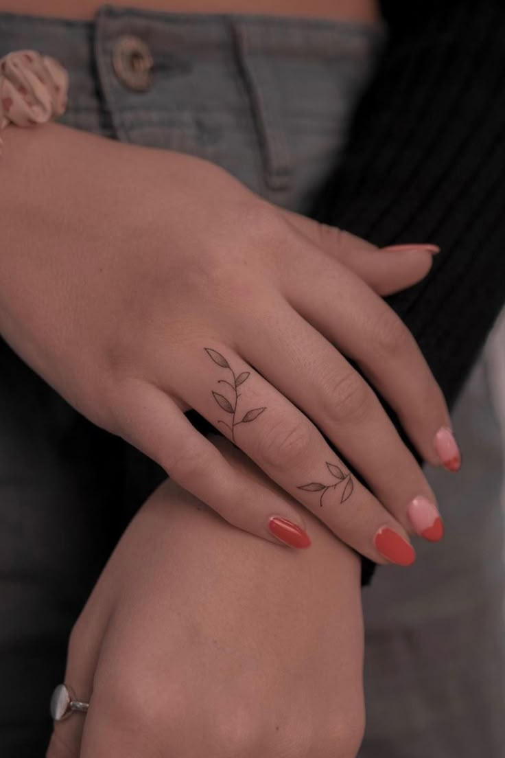 a woman's hand with a flower tattoo on her left wrist and an orange manicure