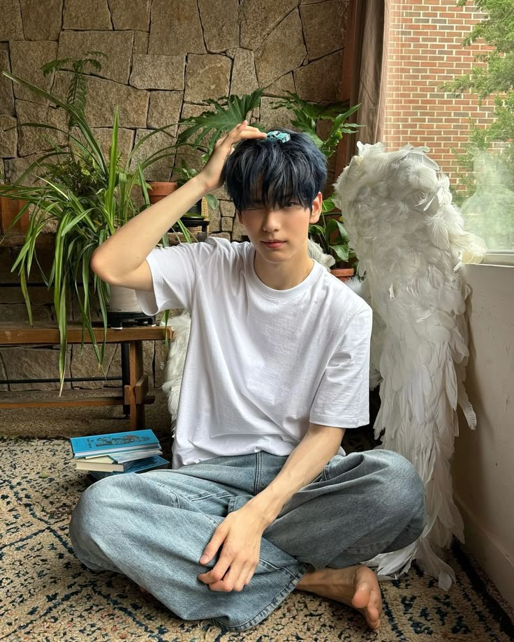 a young man sitting on the floor with an angel wings behind his head and books in front of him