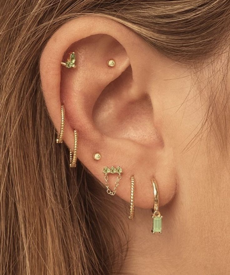 a close up of a person wearing ear rings and piercings with green stones on them