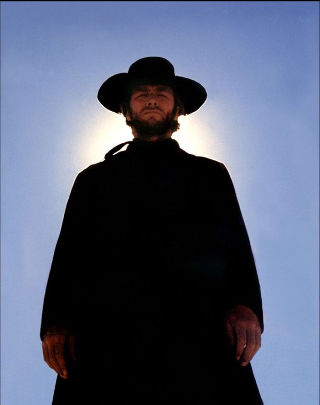 a man wearing a hat and cape standing in front of the sun with his hands on his hips