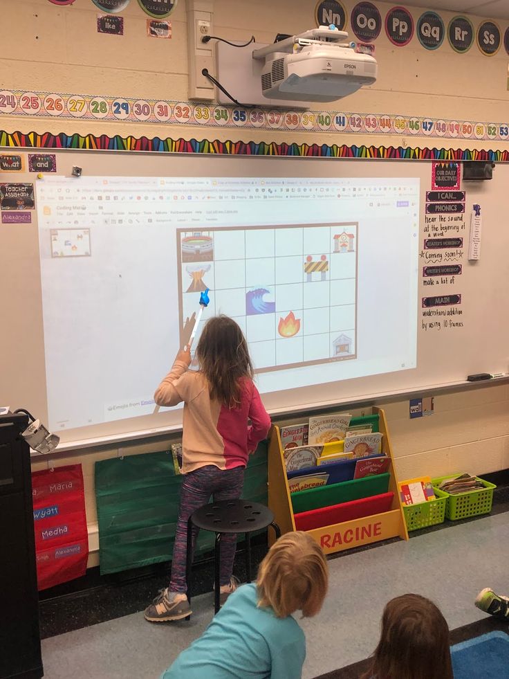 two children are standing in front of a whiteboard while another child is pointing at it