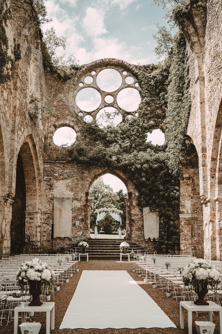 an outdoor ceremony setup with white flowers and greenery on the walls, surrounded by stone arches