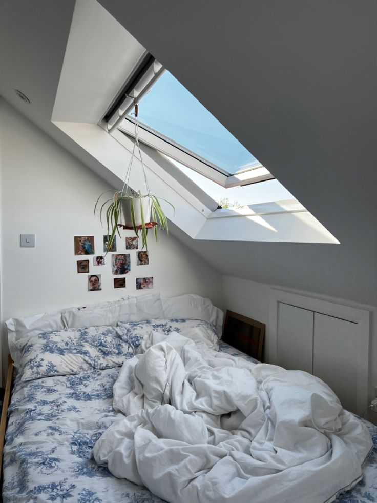 an unmade bed in a loft with skylights and pictures on the wall above it