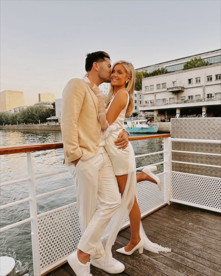 a man and woman are kissing on the deck of a boat in front of some buildings