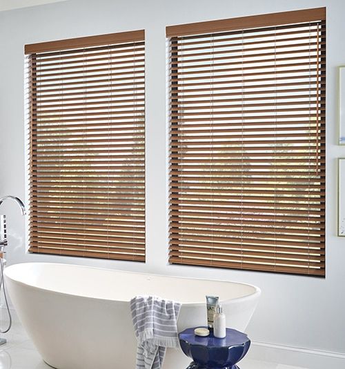 a white bath tub sitting next to two windows with wooden blinds on them in a bathroom