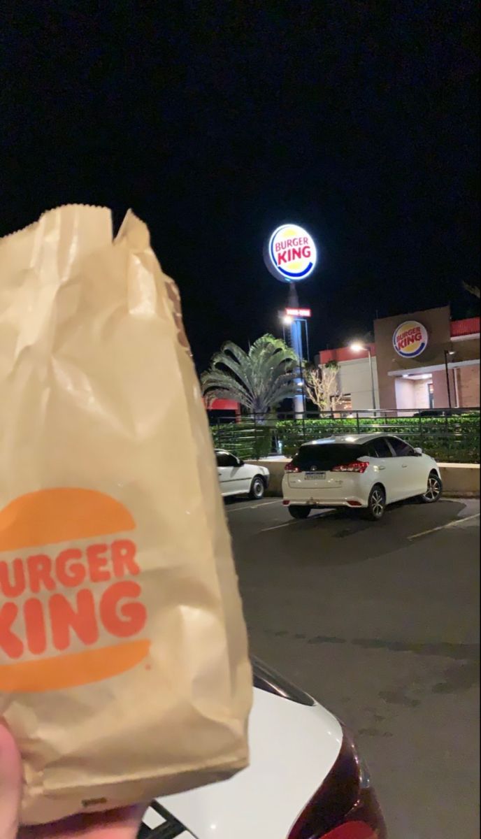 a burger king bag is held up to the camera in front of a parking lot