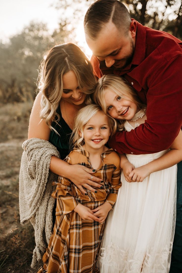 a man and two girls hugging each other while standing in front of some trees with the sun shining on them