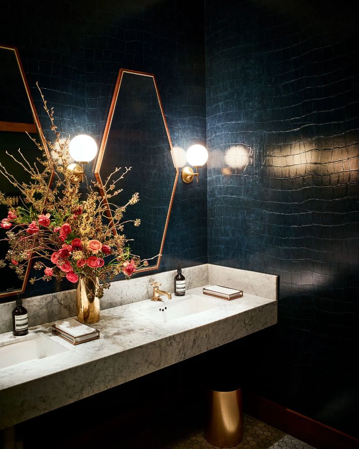 a bathroom sink with two mirrors and flowers in the vase next to it, on top of a marble countertop