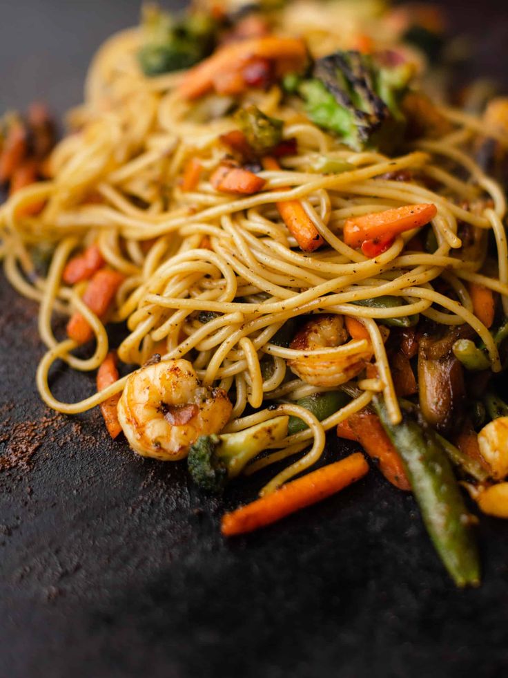 noodles with shrimp, broccoli and carrots on a black plate next to green beans