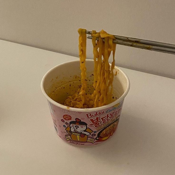 a cup filled with noodles and cheese being held by a pair of chopsticks