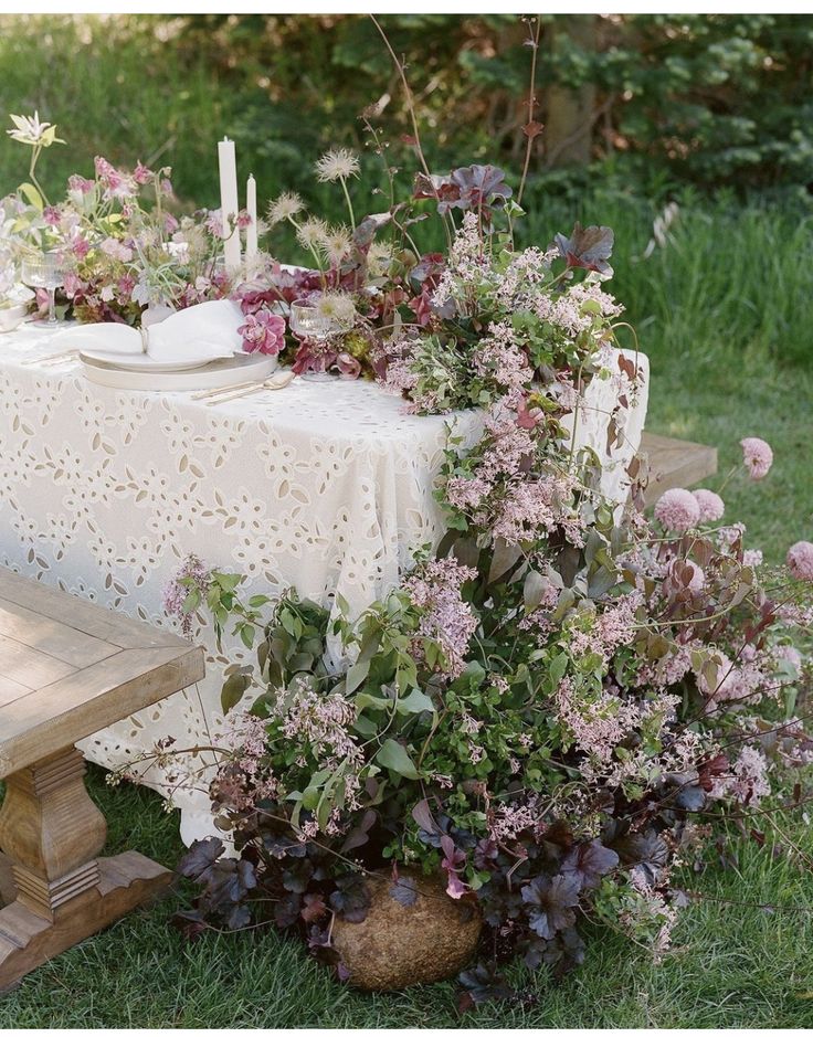 an outdoor table with flowers and candles on it