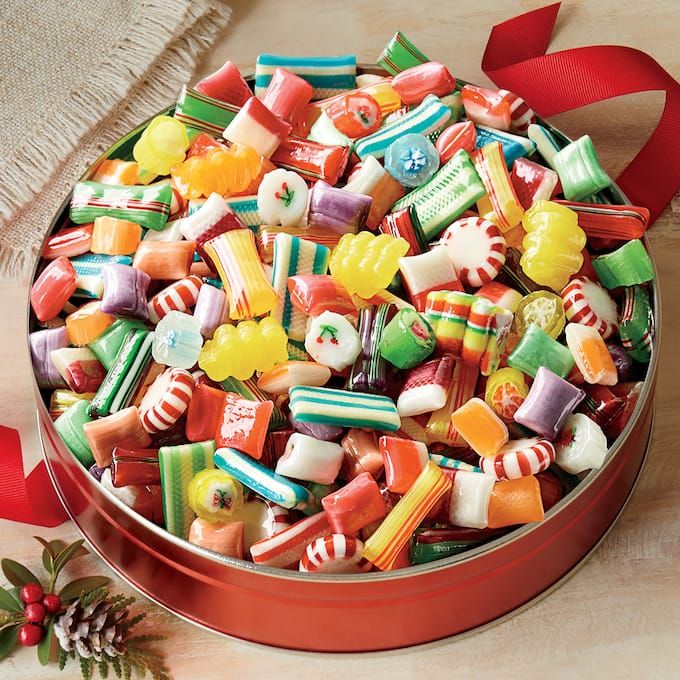 a tin filled with assorted candy on top of a wooden table next to a red ribbon