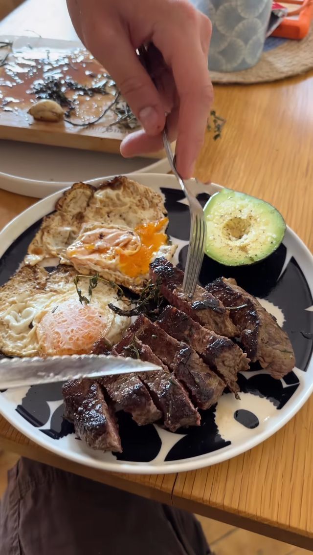 a person is cutting into some food on a black and white plate with an avocado