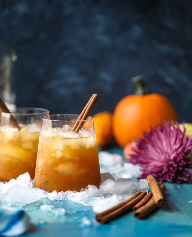 two glasses filled with drinks sitting on top of snow covered ground next to oranges and cinnamon sticks