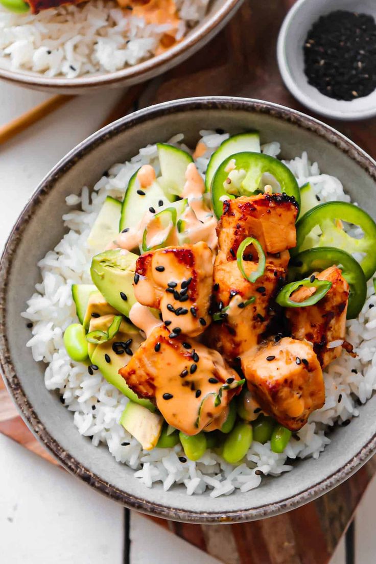 two bowls filled with chicken and cucumber on top of rice