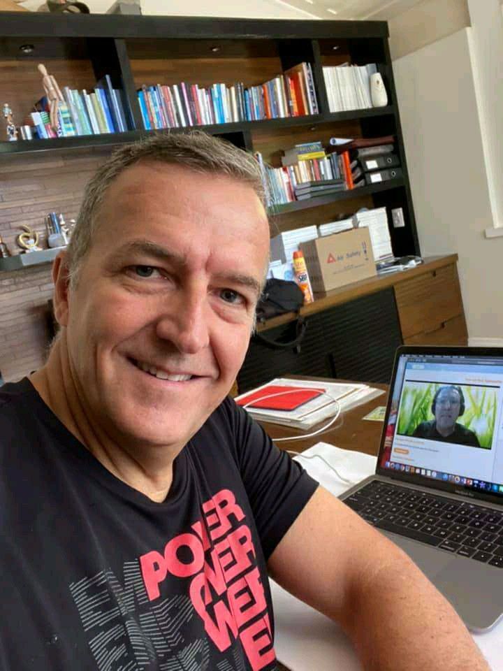 a man sitting at a desk with a laptop computer in front of him and bookshelves behind him