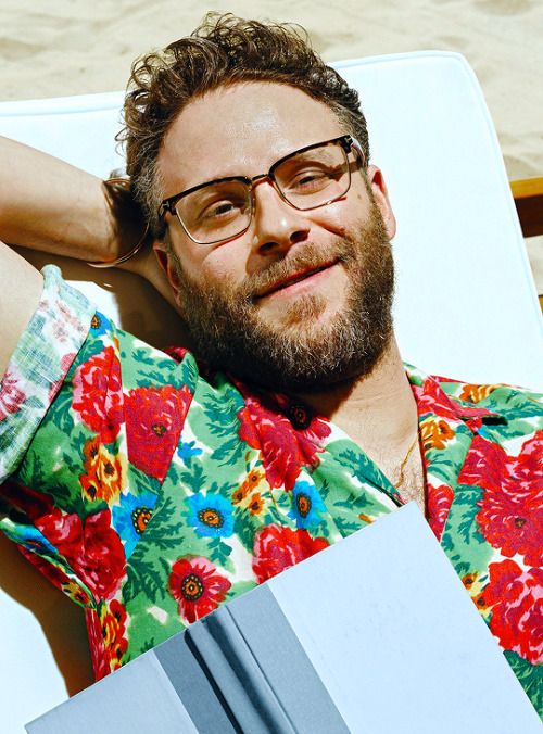 a man with glasses and a beard laying on a beach chair next to the ocean