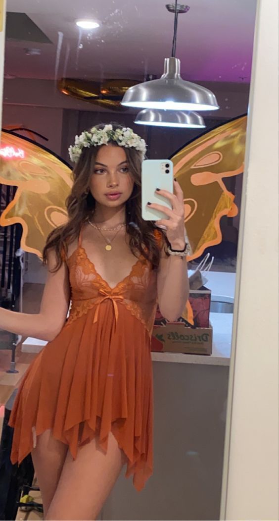 a woman in an orange dress taking a selfie while wearing a butterfly wings costume