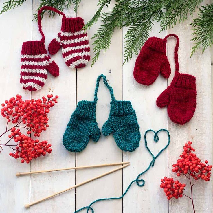 crocheted mittens, gloves and needles on a white wooden surface with red berries