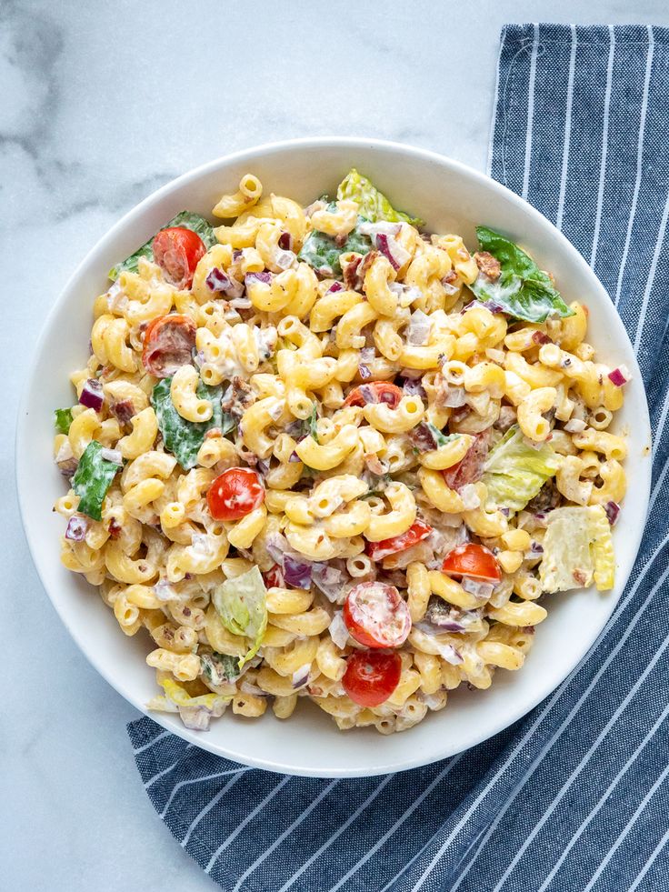 a white bowl filled with pasta salad on top of a blue and white striped napkin