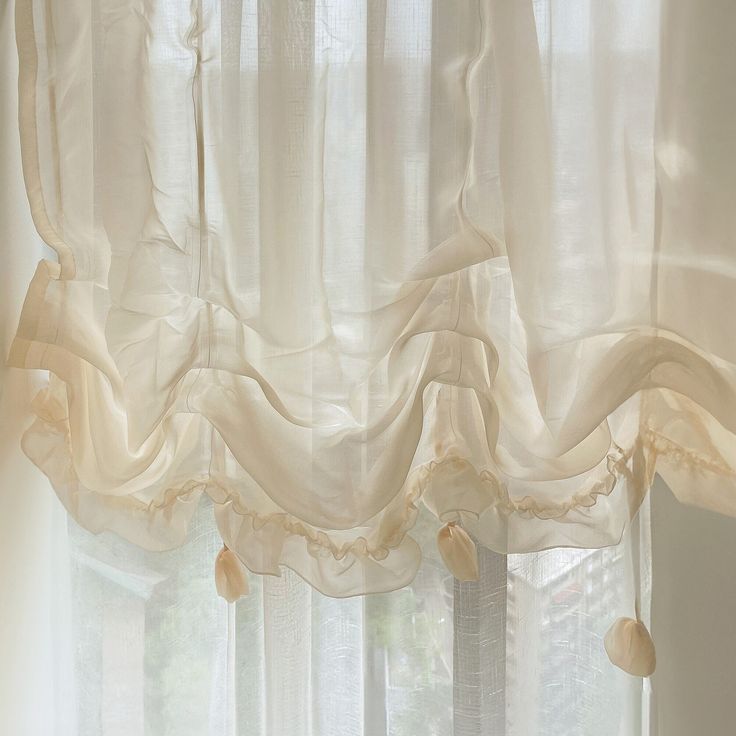 a window with white curtains and shells hanging from it