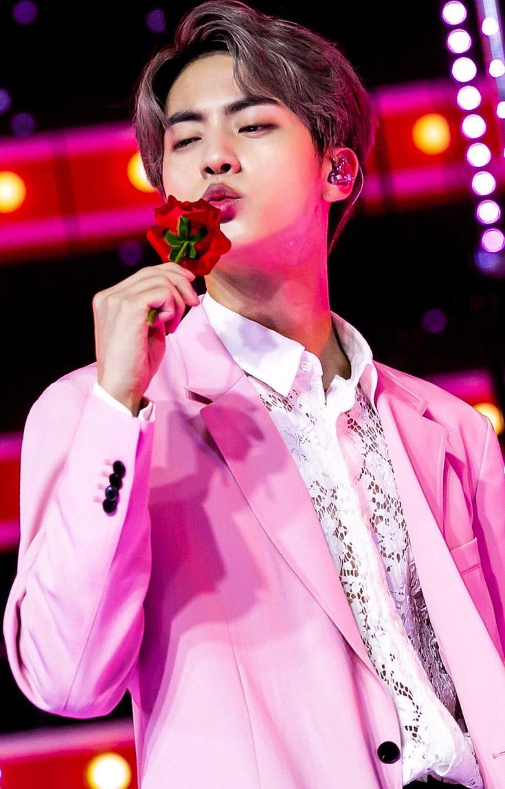 the young man is holding a rose in his hand and wearing a pink suit jacket