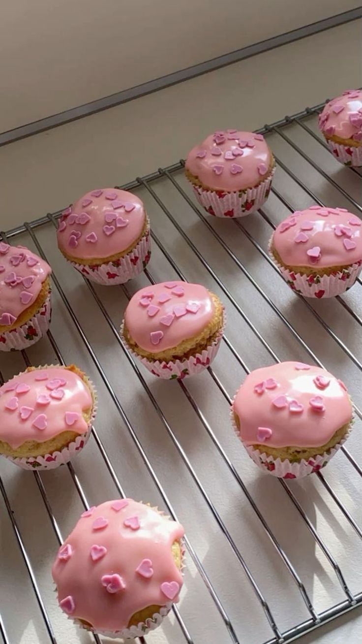 pink frosted cupcakes sitting on top of a cooling rack