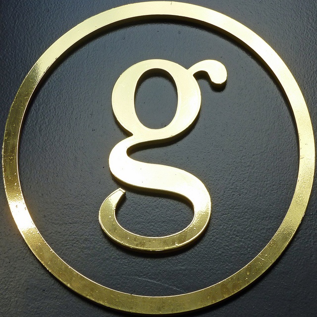 the letter g is inscribed in gold on a black surface