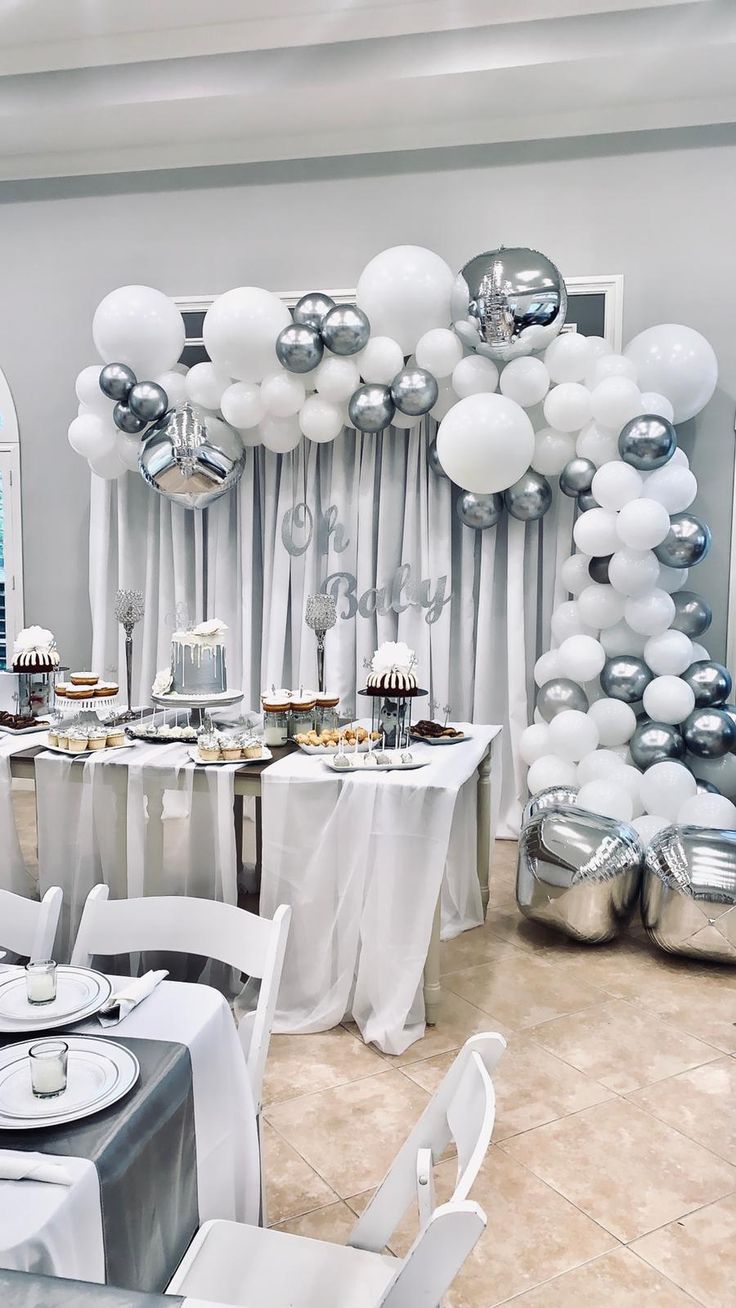 a room filled with tables covered in white and silver balloons