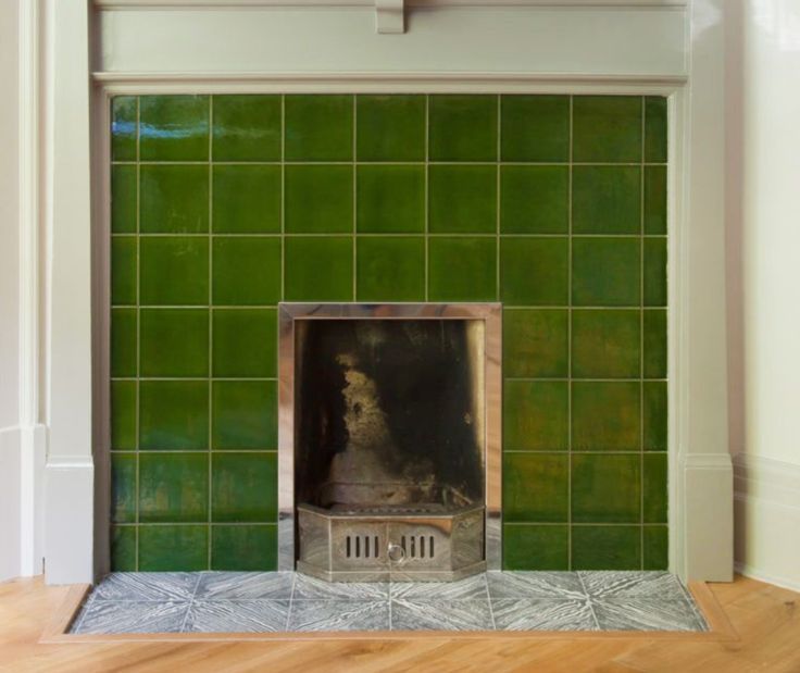 a fireplace in a room with green tiles on the wall and wood flooring around it