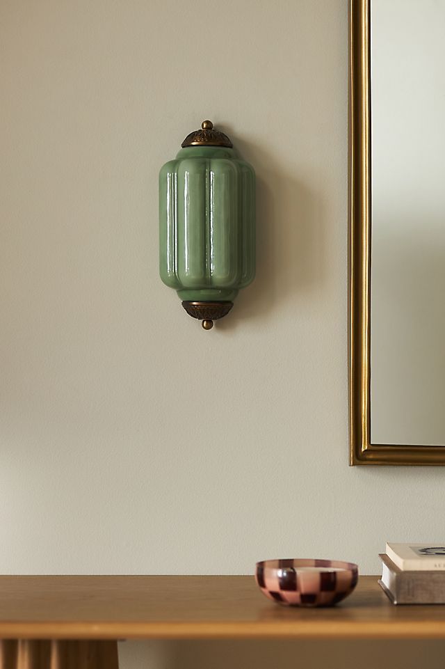 a green vase sitting on top of a wooden table next to a mirror and book